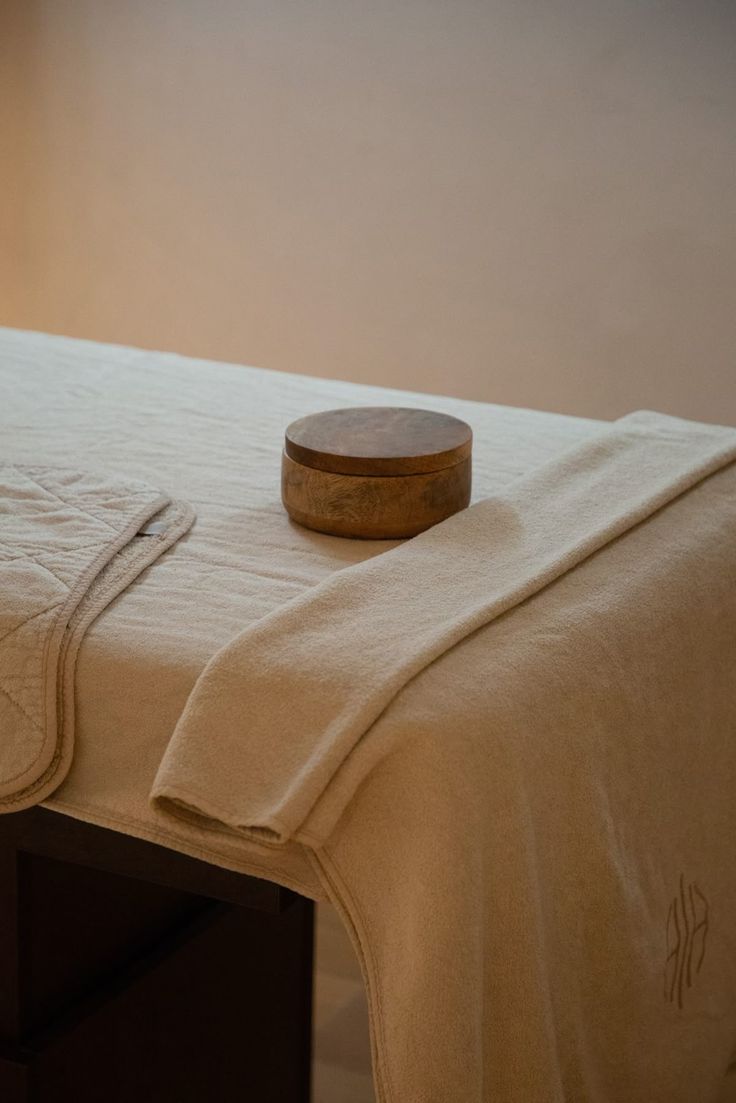 Camilla de tratamiento preparada en casa con textiles naturales y un recipiente de madera para masajes y bienestar